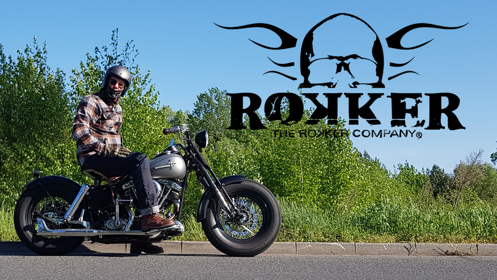 Rokker Company Logo mit Motorrad-Szene Motorradfahrer mit Jeans und Rider Shirt von Rokker sitzt auf einer klassischen Maschine, daneben das Logo von The Rokker Company mit Totenkopf und Flügeln